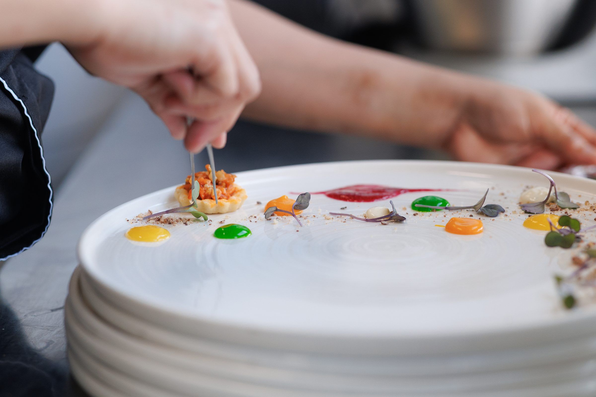 A chef plating a dish with sauces and garnish