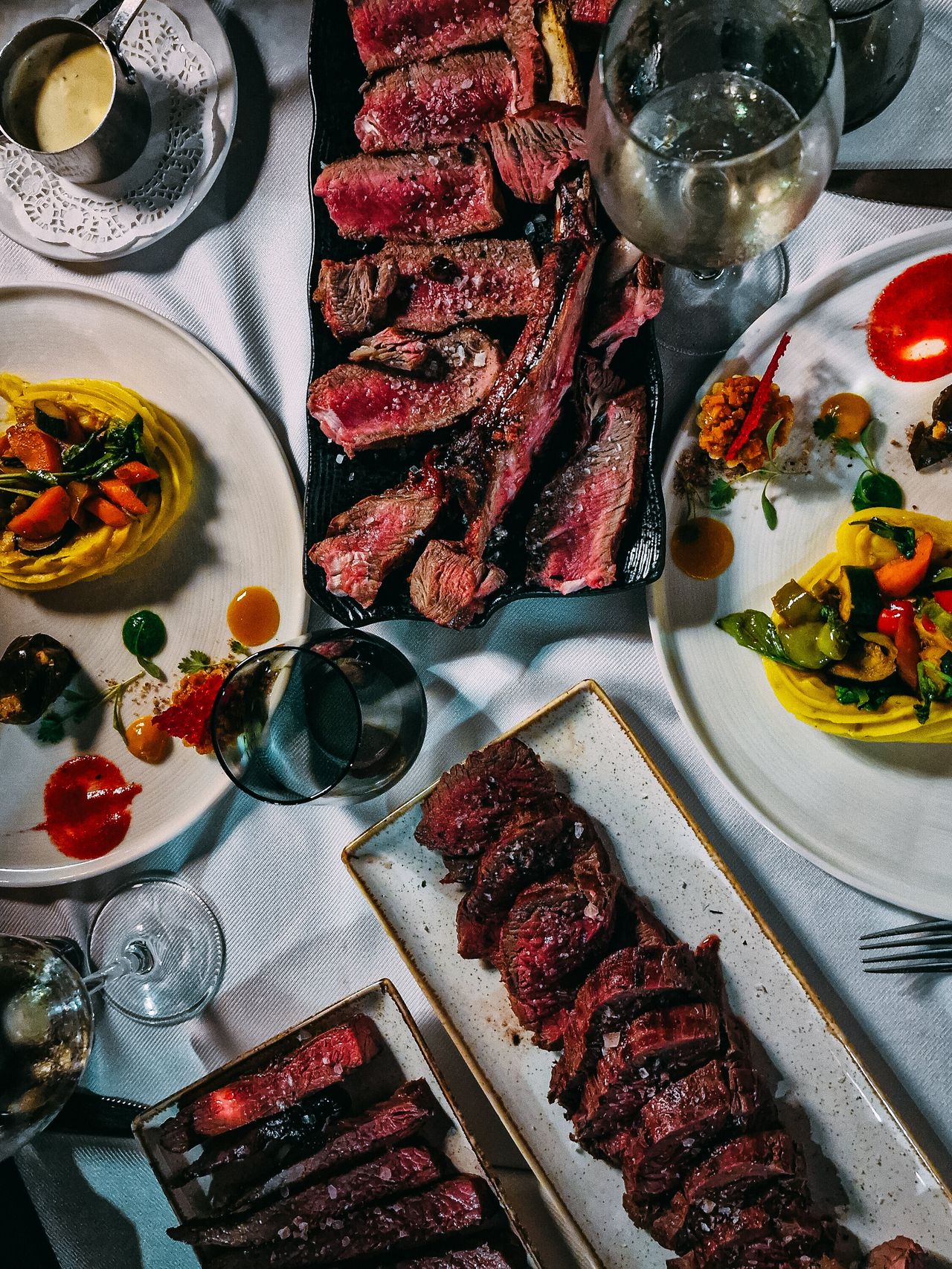 A table seen from above with platters of sliced steak, Mediterranean plates and wine