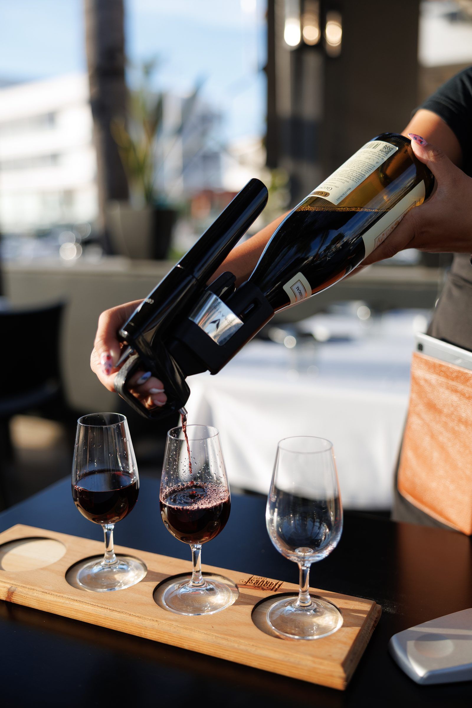 A server pouring red wine into a row of glasses